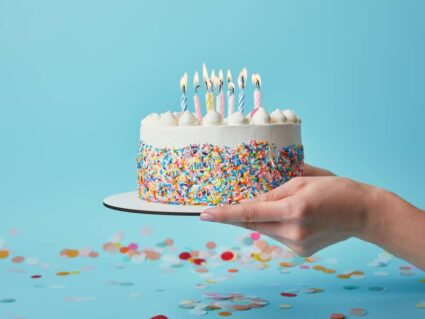 Verjaardagstaart Verjaardagstaart met kaarsjes, vastgehouden door twee handen voor een blauwe achtergrond